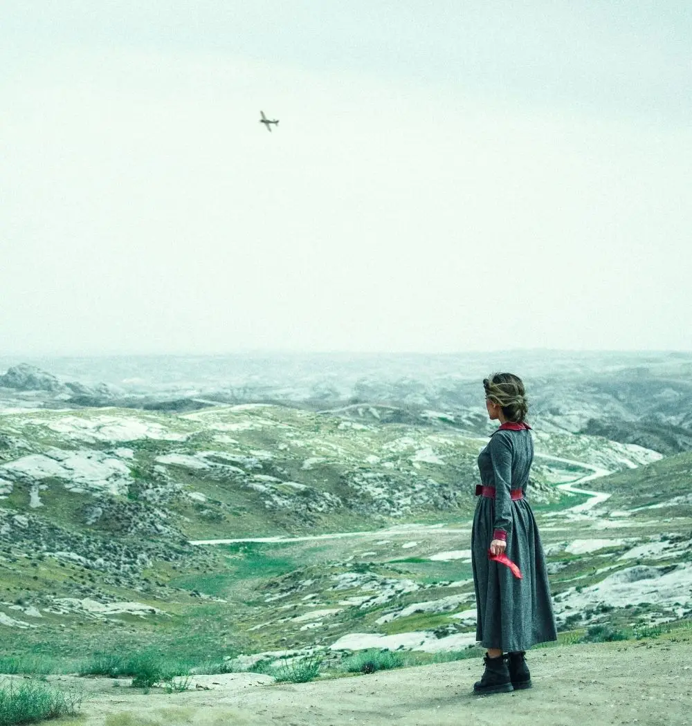 world war 2 woman standing on cliff watching war plane in distance