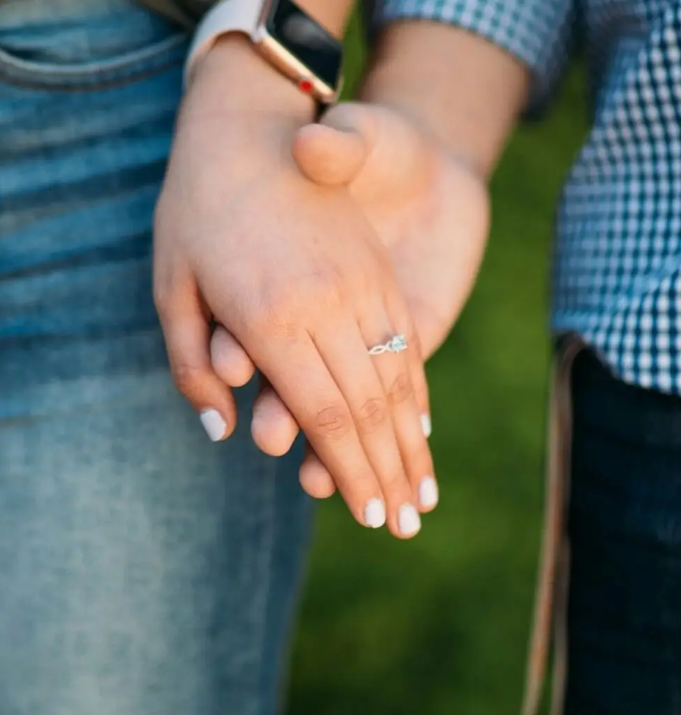 young couple showing engagement ring while holding hands