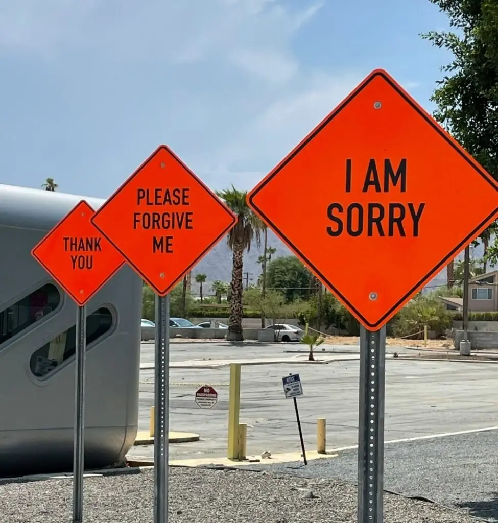bright orange road signs with "i am sorry" and "please forgive me" in black text