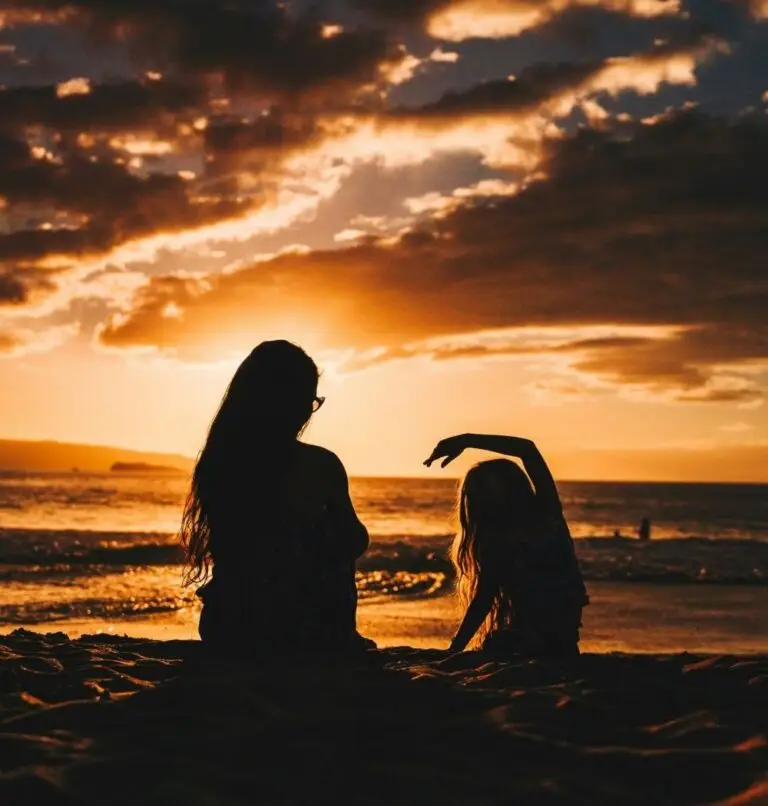 Mother and daughter on beach reading Bible at sunset