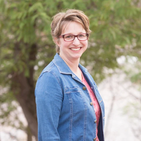 image of bestselling author naomi rawlings - woman with short light brown hair, glasses, denim shirt standing in front of a tree