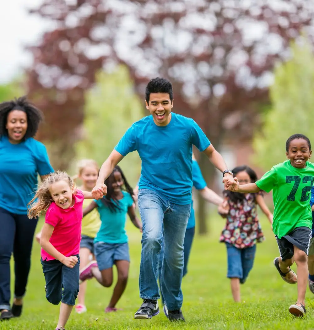 Kids and camp counselors running across field at vacation Bible school