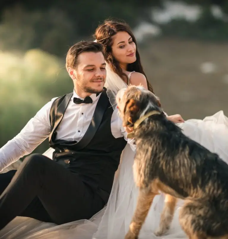 Newlywed bride and groom sit with their dog outside