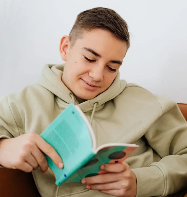 teen boy in hoodie smiling and reading Christian fiction book