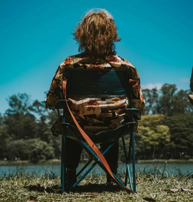 young man sitting on camping chair enjoying nature with a lake and blue sky