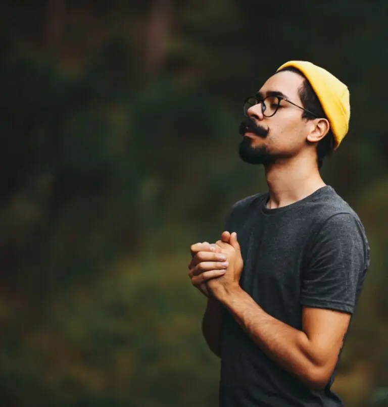 young christian man with his hands clasped in prayer in the forest