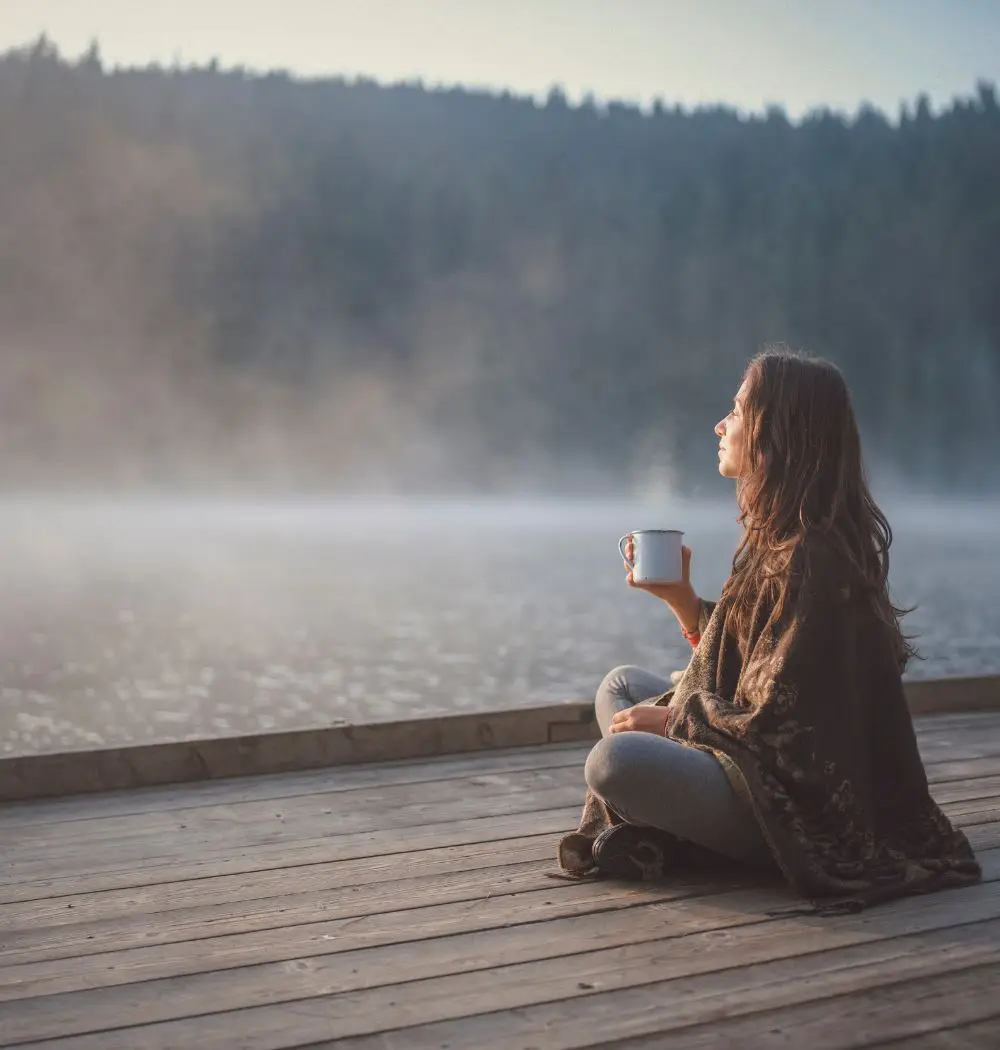 woman relaxes with cup of tea on lakeside dock after reading an inspiring Christian devotional