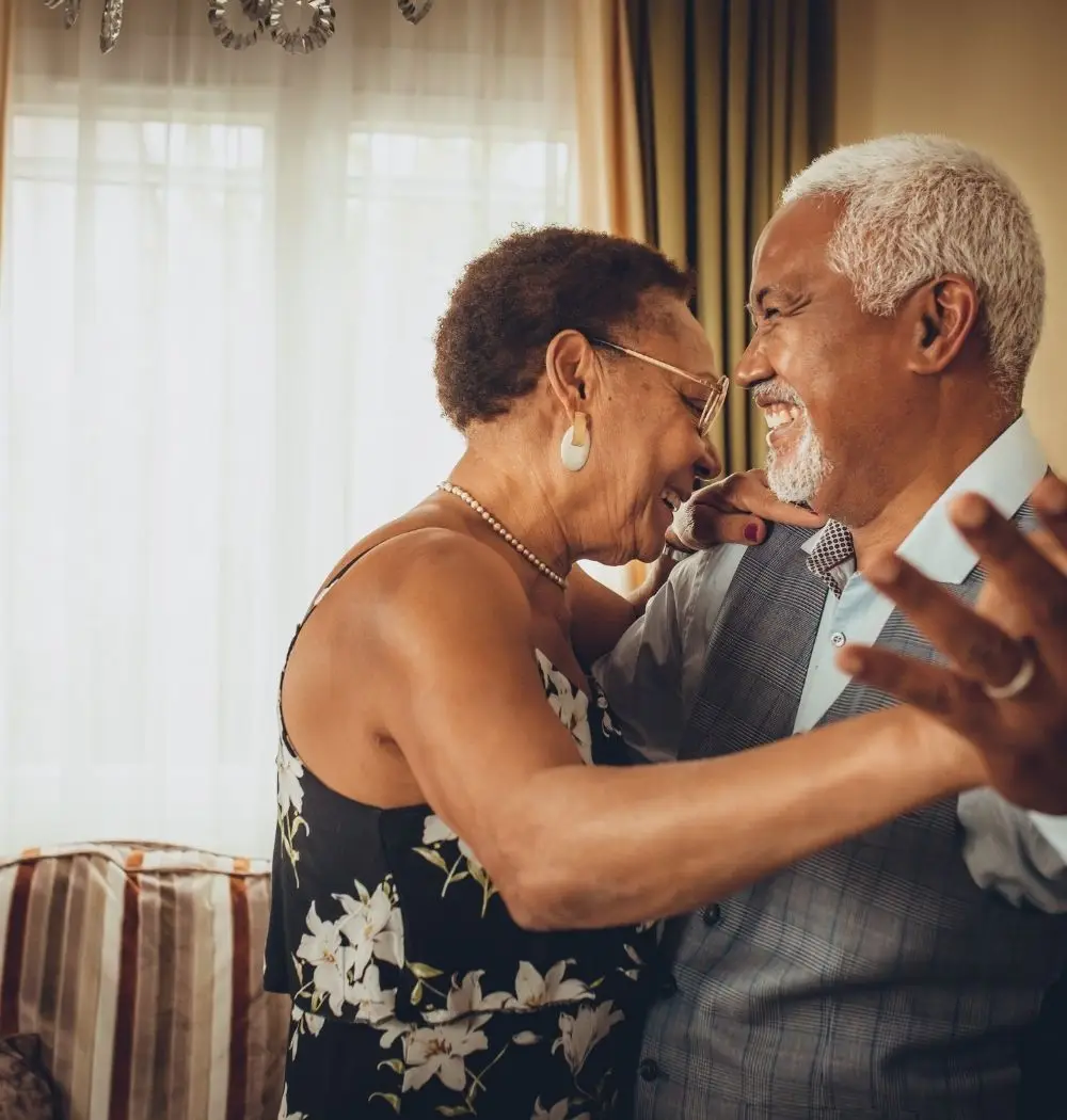 older Christian couple dancing and smiling in living room