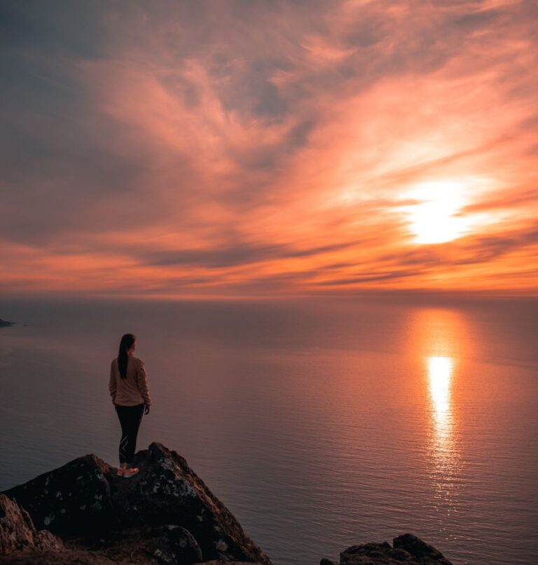 Christian curious woman standing on seaside cliff looking at the sunset