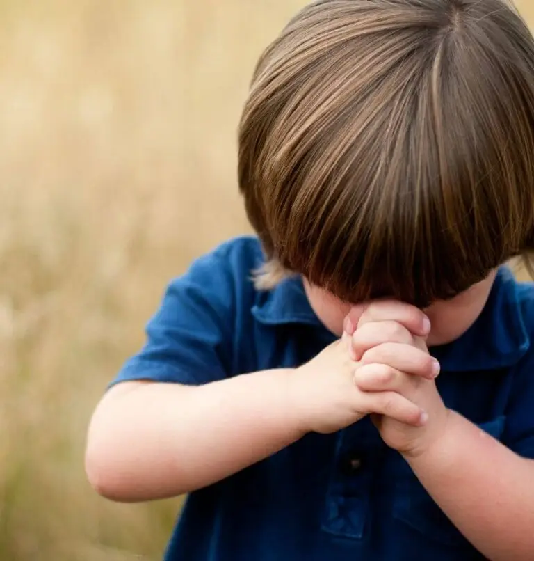 Young boy praying to God with his hands clasped near his face