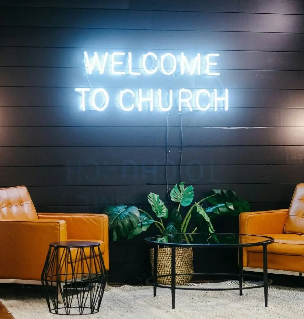 two chairs on a stage with a neon sign that says welcome to church